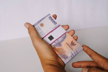 Bir avuç Endonezya Rupia banknotunu tutan bir elin yakın çekimi. Görüntü, Endonezya ile ilgili mali temaları vurguluyor, para, ekonomi ve zenginlik, yatırım ve ticari işlemler kavramlarını gözler önüne seriyor.