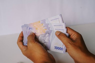 Endonezya Rupiah banknotlarını tutan ellerin yakın çekimi. Ellere ve 10000 IDR para birimine odaklanın. Finansal işlemler ve zenginlik sergileniyor. Ekonomi, yatırım ve Endonezya finans piyasası ile ilgili kavramların resmedilmesi için uygun