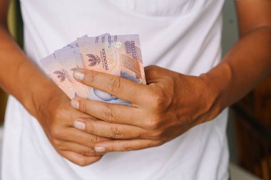 Endonezya Rupia banknotlarını tutan bir adamın yakın çekimi. Mali refahı, yatırımı ve Endonezya 'nın büyüyen ekonomisini sembolize ediyor. Zenginliği ve başarılı mali yönetimi temsil eder.