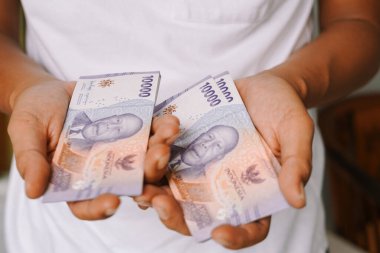 Endonezya Rupiah nakit parasının bir kişi tarafından tutulduğu yakın plan. 10,000 Rupiah banknotları ellerinde sergileniyor, para ve finansal kavramlar sergileniyor..