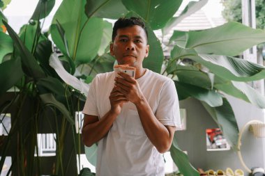 Elinde bir yığın Endonezya Rupiah banknotları tutan adam. Açık hava ortamında tropikal yapraklarla çevrilidir. Bu görüntü Endonezya 'da zenginliği, yatırımı veya ekonomik başarıyı temsil edebilir..