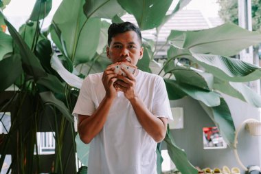 Genç bir adam bir yığın Endonezya Rupiah banknotunu elinde tutuyor. Görüntü zenginlik, başarı ve finansal refah duygularını iletir. Çevredeki yemyeşil alan büyümeyi ve refahı temsil edebilir..