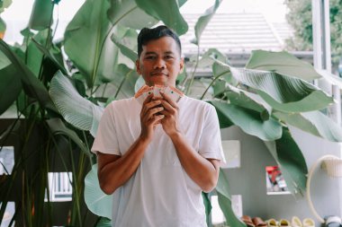 Neşeli genç bir adam Endonezya Rupiah banknotlarının hayranı, başarı ve refah saçıyor. Çekim açık havada, yemyeşil tropikal yaprakların arasında yapılır..