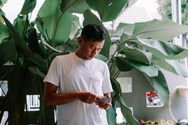 Tropik yeşilliklerle çevrili bir Asyalı adam dikkatlice banknotları sayıyor. Mali işler, bütçe yönetimi veya mali konuların doğal ortamında ele alınmasına odaklanmış görünüyor. Görüntü zenginliğin temaları, zenginliğin