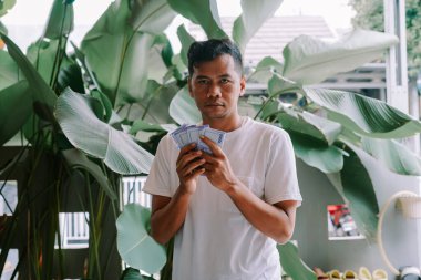 Adamın biri elinde bir yığın Endonezya Rupia banknotuyla yemyeşil tropikal bitkilerin önünde duruyor. Güneydoğu Asya 'da zenginlik, mali başarı ve yatırım potansiyeli gösteriyor. Kazanç gücü, tasarruf veya son mali işlemleri temsil eder.