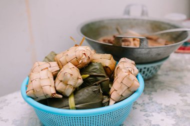Mavi sepette ketupa yakın çekim ve bir tabak. Ketupat, bazı güneydoğu Asya ülkelerinde bayram sezonlarında popüler olan geleneksel bir pirinç köftesidir. Genellikle ramazan ve bayram kutlamalarında yenir..