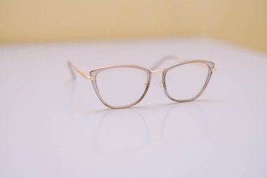 Altın çerçeveli şık bir gözlük temiz, beyaz bir yüzey üzerinde sergilenir. Tasarım modern ve zarif, moda, güzellik veya optikle ilgili projeler için uygundur. Minimalist arka plan, aksesuarın estetiğini vurgular..