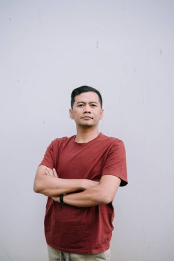 Kolları tarafsız bir zemin üzerinde katlanmış, sakin ve ciddi bir ifade sergileyen düşünceli Asyalı bir adam.