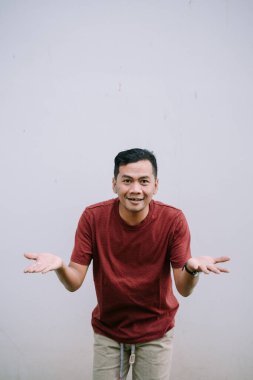 Asyalı genç adam şaşkın bir ifadeyle omuz silkiyor. Belirsiz ya da şüpheli davranışlar sergiliyor.