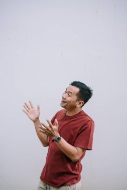 Heyecanlı bir adam, sıradan giyinmiş, elleriyle arka planda el kol hareketi yapıyor. Sürpriz ve mutluluğu yansıtan bir portre.