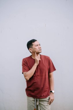 Düşünceli Asyalı adam elleri çenesinde, düşüncelere dalmış ve duvarın arkasına yan bakıyor.