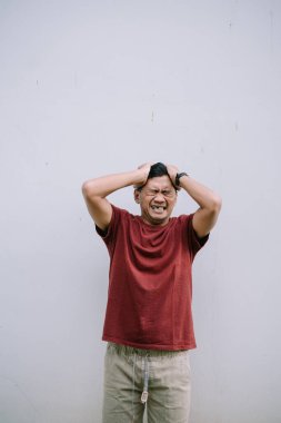 Gergin bir adam stres yaşıyor, elleriyle kafasına dokunuyor, hayal kırıklığını ifade ediyor. Duvara yaslanmış.