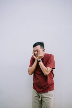 Dayanılmaz diş ağrısı olan stresli Asyalı bir adam iki eliyle dış duvarlara tutunuyor.