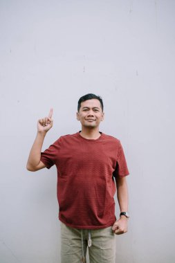 Gülümseyen Asyalı bir adam, metin veya grafik ögesi için yukarıdaki dokulu bir duvara işaret eder.