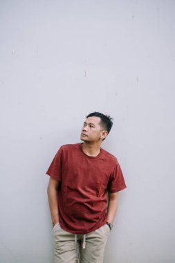 Sıradan giyinmiş bir adam beyaz bir duvara doğru eğiliyor, dikkatlice yukarı bakıyor. Açık hava çekimi.