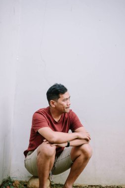 Düşünceli bir adamın portresi beyaz bir duvara yaslanmış kollarıyla çömelmiş, düşüncelere dalmış.