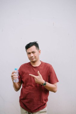 Kırmızı tişörtlü bir adam su şişesini tutuyor ve onu işaret ediyor. Sıvının sağlıklı bir yaşam tarzı için önemini destekleme kavramı