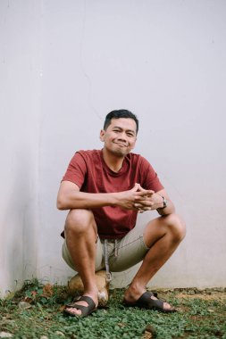 Gülümseyen ve rahat Asyalı bir adamın portresi duvarın önünde oturuyor, evinin arka bahçesinde huzuru ifade ediyor.