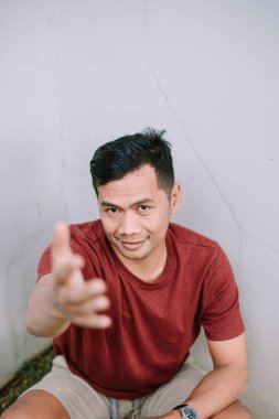 Neşeli adam elini uzatıyor ve düz bir duvara karşı poz veriyor. Sıradan, çekici ve arkadaş canlısı..