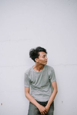 Genç Asyalı bir adam beyaz bir duvarın önünde duruyor, derin derin düşünüyor. Modern, içsel ruh hali üzerine bir çalışma..