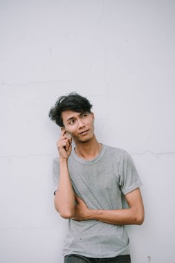 Gri gömlekli düşünceli genç bir adam beyaz bir duvara yaslanırken bir fikir düşünüyor.. 