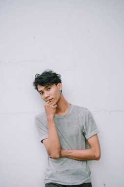 Gri tişörtlü içe dönük genç bir adam, düşüncelere dalmış, dokulu bir duvara karşı, düşünce ya da modern yaşam tarzı için mükemmel.