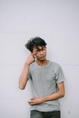 Düşünceli Asyalı bir adam beyaz desenli arka planda gözüne dokunuyor. Yakın çekim portresi içgözlem duygusunu yansıtır.