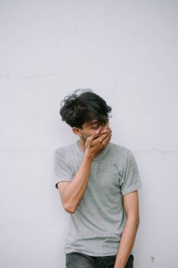 Stresli genç bir adam ağzını kapatır, dokulu bir duvara karşı endişe ve endişe gösterir. Endişelerini ve umutsuzluklarını dile getiriyor..