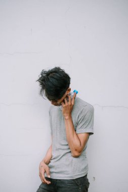 Günlük giysiler içinde genç bir adam dinleniyor, boynuna su şişesi dayayıp dokulu duvarda, düşünceli bir duraksama ve kişisel bakım sahnesini canlandırıyor..