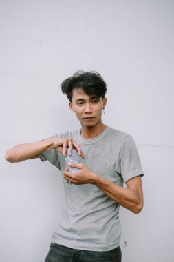 Gri gömlekli susuz Asyalı bir adam su şişesini açıyor. Açık hava ortamında susuzluğa hazır.