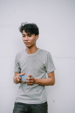 Gri tişörtlü genç bir adam beyaz bir duvara bir şişe su tutuyordu, düşüncelere dalmıştı..