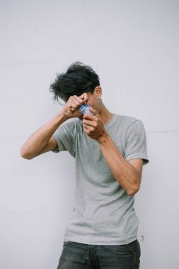 Genç bir adam, susuzluğunu gidermek için günlük susuzluk ve kararlılığını gösteren tarafsız bir arkaplanda su şişesini açmaya çalışıyor.