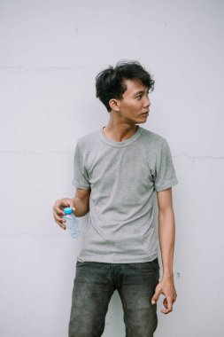 Elinde su şişesi olan genç bir adam düşünceli bir ifadeyle dokulu bir duvara bakıyor..