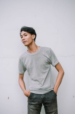 Sıradan giyinmiş genç bir Asyalı düz bir duvara karşı güvenle poz veriyor. Onun modern tarzı basitlik ve kentsel eğilimin bir karışımıdır..