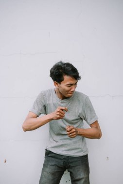 Giyim kuşamında gergin genç bir adam titiz beyaz bir duvara karşı gergin bir şekilde el kol hareketi yapıyor. Endişe, stres ya da gerginlik belirtileri gösteriyor.