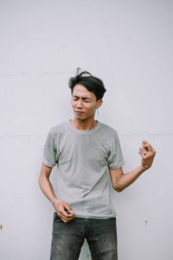 Etkileyici genç bir adam beyaz bir duvar arkasında jest yapıyor. Sıradan giyinmiş bir adam, el ve yüz ifadeleriyle duygularını gösterir..