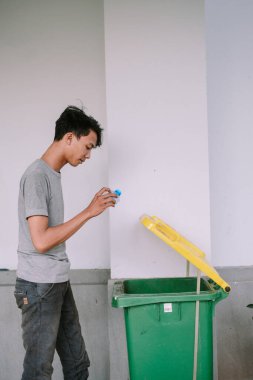 Genç adam plastik şişeyi geri dönüşüm kutusuna atıyor, daha temiz bir çevreye katkıda bulunarak sorumlu atık yönetimi uygulaması yapıyor.