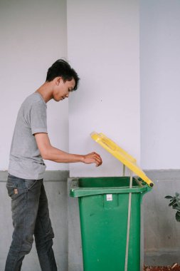 Genç adam çöpü yeşil geri dönüşüm kutusuna atıyor. Atık yönetimi ve çevre sorumluluğu için günlük faaliyet. 