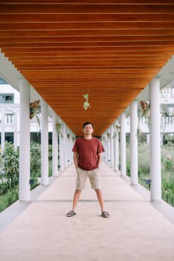 Genç adam, sallanan bitkilerle eşsiz ve simetrik bir geçidin altında durup poz veriyor ve huzurlu bir ortam yaratıyor.