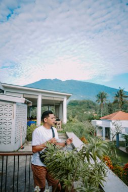 Adam huzurlu bir sabahta balkondan manzaranın keyfini çıkarıyor. Tatil sırasında bir içeceğin tadını çıkarıyor.