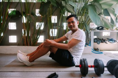 Asyalı bir adam spor salonunda halterlerle egzersiz yaptıktan sonra dinleniyor. Sağlıklı yaşam tarzı. 