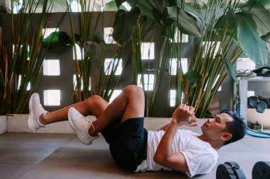 Evde egzersiz paspası üzerinde mekik çeken bir adam. Bitkilerle aydınlık ve rahat bir alanda egzersiz yapmak. Sağlıklı yaşam tarzı ve ev çalışma konsepti.