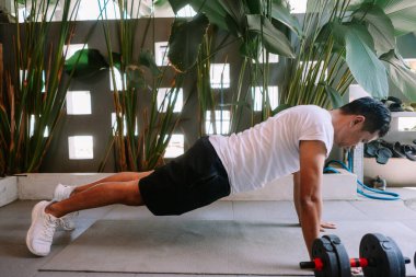 Spor giysili Asyalı bir adam evdeki minderde şınav çekiyor. Tropik bitki arka planı. Ev çalışması kavramı.