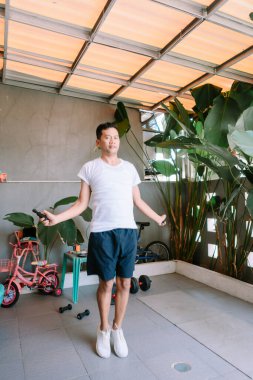 Aktif Asyalı adam ip atlıyor. Gündüz vakti arka bahçede antrenman yapıyor.