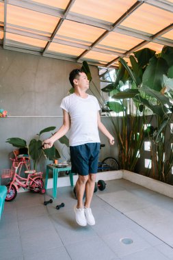 Arka bahçede ip atlarken kardiyo antrenmanı yapan genç bir adam. Sağlıklı bir yaşam tarzı için içeride spor aktivitesi.