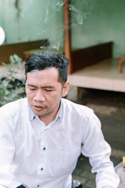 Düşünceli bir adam, sigara dumanı yükseliyor, düşüncelerde kayboluyor. Stresi, alışkanlığı ya da derin düşünmeyi temsil eder..