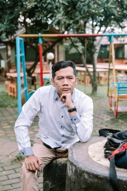 Sigara içen ve çocuk parkında düşünceli görünen bir adam. Dinleniyor ve ara veriyor..