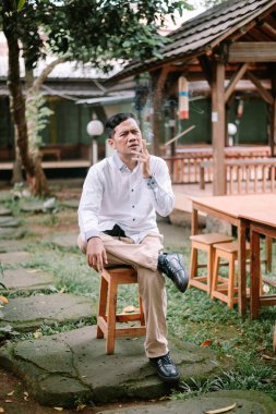 Günlük kıyafetli bir adam, düşünmek için biraz zaman ayırıyor, bahçedeki bir sigaranın tadını çıkarıyor.