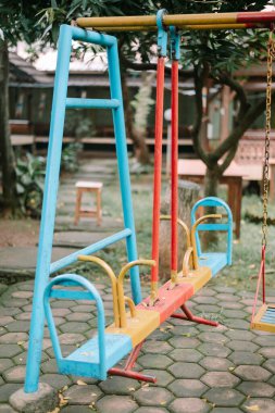 Canlı, yaşlı oyun parkı tahterevalli salıncak, yapraklı bir alanda hareketsiz duruyor, çocukluk anlarına nostaljik bir bakış sunuyor ve açık hava eğlencesi ve hatıraların basitliği.
