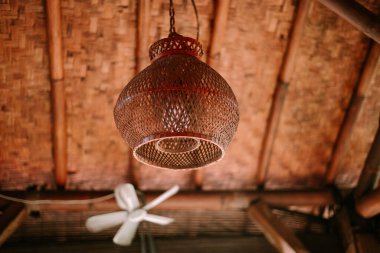 Dekoratif örülmüş bir kolye, dokulu bambu tavanının altında asılı, sıcak, kırsal bir ortam yaratıyor..